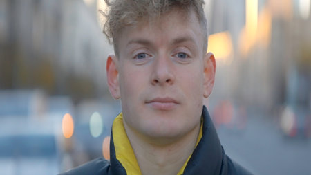 Close-up of man looking at camera on background of city. Action. Attractive young man looks at camera on street. Portrait shooting of young man on blurred background o busy cityの写真素材