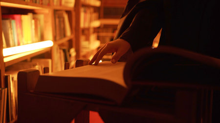Close-up of mysterious man opening large book. Stock footage. Man opens book in dark library with flashing light. Secret society with mysterious books in night libraryの写真素材
