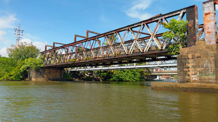 Ancient iron bridge over river. Action. Rusty old bridge over river in tropical area. Iron bridge over river in tropics on sunny summer dayの写真素材