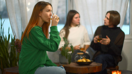 Students talk and relax in cozy cafe. Media. Beautiful young woman is drinking tea on background of talking couple. Students relax and drink tea in college cafeの写真素材