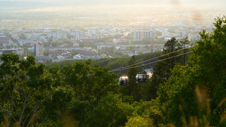 Beautiful view of cable car with view of town in summer. Clip. Green forest on slope with moving...