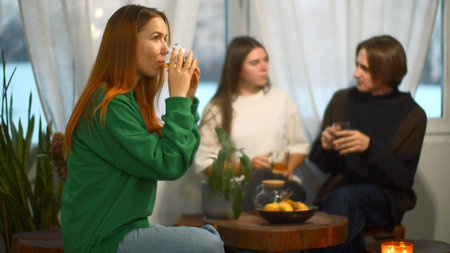 Students talk and relax in cozy cafe. Media. Beautiful young woman is drinking tea on background of talking couple. Students relax and drink tea in college cafeの写真素材