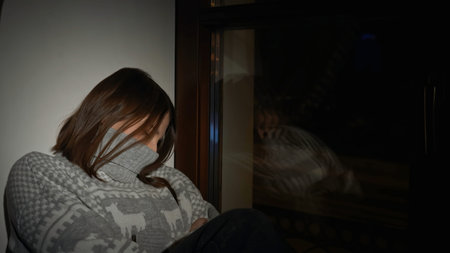 Sad sleepy woman sitting at home by the window. Media. Lonely girl in dark apartment in grey...