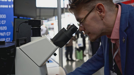 Man looks through microscope. Media. Man looks through new microscope at technology exhibition. New...