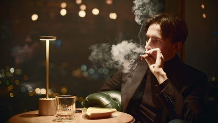 Young man smokes cigar in restaurant. Media. Elegant man in suit smokes cigar in restaurant. Mafia...