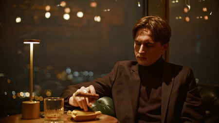 Young man with cigar in restaurant. Media. Young man in suit learns to smoke cigar in restaurant....