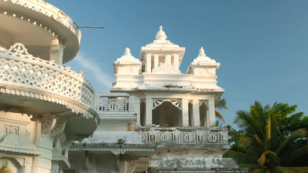 White Indian Temple with palm tree. Action. Beautiful white temple with Buddhist patterns. White Buddhist temple with palm trees on sunny summer dayの写真素材