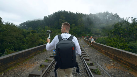 Man on hiking trip on tropical bridge. Action. Man on hiking trail with stone bridge and railway....