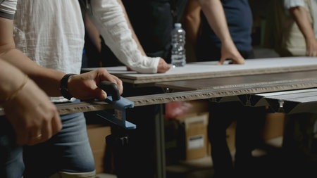 Woodworking master class. Creative. Close-up of man shows group of people how to take measurements on wooden board. Master class in carpentry in industrial workshopの写真素材