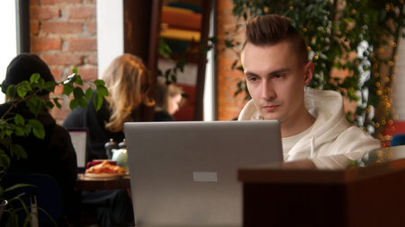 Young man is concentrating on laptop in cafe. Stock footage. Student is writing paper on laptop in...