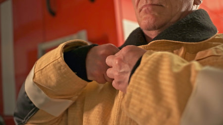 Mature professional fireman getting dressed. Clip. Man wearing protective uniform for the emergency call.の写真素材