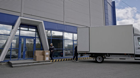 View outside of logistics retailer warehouse, loading goods process. Media. Workers putting large...