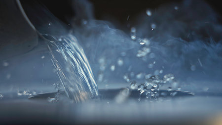 Hot water being poured out of bucket. Stock footage. Close-up of jet of water pouring out of small bucket. Hot clean water is poured from ladle into metal container with steamの写真素材