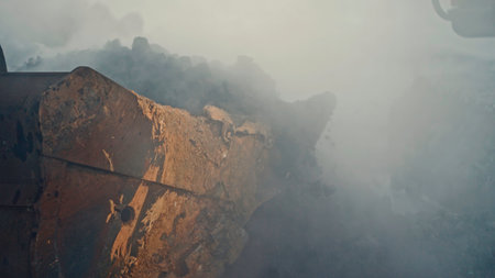 Rotating excavator in industrial dust at quarry. Stock footage. Cinematic video of industrial excavator in cloud of dust at quarry. Excavator rotates and rakes in minerals at quarryの写真素材