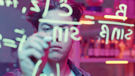 Young man solves mathematical equations on blackboard. Media. Young man solves complex equations on blackboard. Genius writes equations on blackboard in neon lightの写真素材