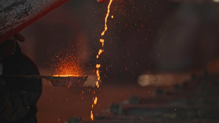 Jet of red-hot metal pours at factory. Stock footage. Beautiful red-hot metallic liquid is poured onto molds to solidify. Metallurgical plant with incandescent metal streamsの写真素材