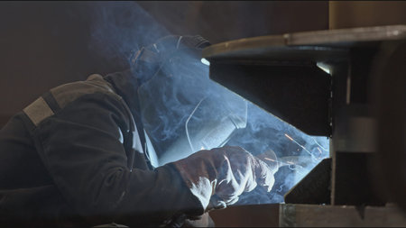 Welder welds metal structures at factory. Stock clip. Masked welder is working on assembly of metal...