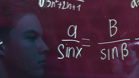 Young man solves equations. Media. Close-up of young mans reflection on transparent writing board...