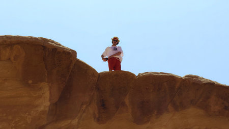 An Adventurer Standing on a Majestic Rock Formation Beneath a Clear Blue Sky Expansively. Actionの写真素材