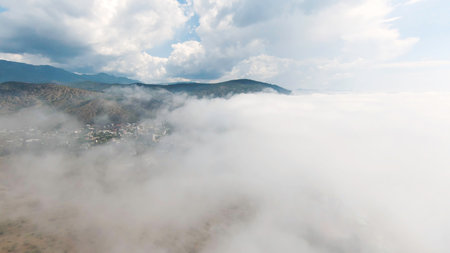 Top view of thick clouds with mountain peak on horizon. Flying in cloudy sky with dense clouds from top of mountain. Landscape of top of green mountain on horizon among white cloudsの写真素材