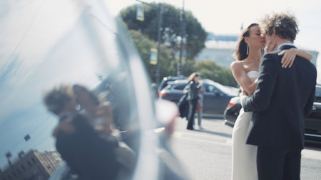 Beautiful newlyweds in reflection of car. Action. Newlyweds are hugging on city street with reflection in car windows. Reflection in car window of couple in loveの写真素材