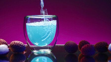 Blue drink is poured into glass on isolated background. Stock clip. Carbonated blue drink is poured into clear glass in bar. Bright drink with ingredients and fruits aroundの写真素材