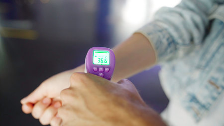 Checking fever of a visitor with a digital thermometer in the wrist area. Concept of protect from Coronavirus, COVID 19 outbreak and healthcare.の写真素材