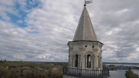 Countryside landscape with an old white tower surrounded by small town and forest on blue cloudy sky background. Stock footage. Aerial of the abandoned old tower, architecture concept.の写真素材