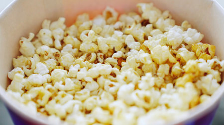 Close up of male hand taking popcorn from a bucket, concept of cinema. Media. Man hand taking sweet delicious popcorn from a dark blue bowl.の写真素材