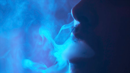 The mouth of a young man smoking the traditional hookah in the dark room, bad habits concept. Action. Close up of male face detail, exhaling smoke.の写真素材