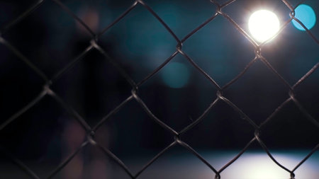 Close up of chain link fence on dark blurred background with shining lamp. Video. Metal lattice inside the building.の写真素材