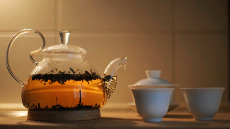 Teapot with fresh tea leaves in hot water and small cups on the kitchen table. Concept. Close up of glass transparent teapot with brewing black tea, concept of tea ceremony.の写真素材