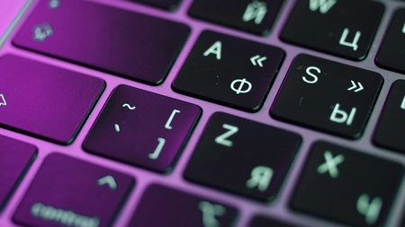 Close up of laptop or computer keyboard. Action. Concept of modern devices and technologies, buttons of a black keyboard under the purple light.の写真素材