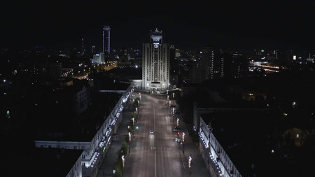 Aerial view of one of the central street in Ekaterinburg city at night. Stock footage. Flying along the houses decorated by shining lights towards the high rise building with unusual roof, concept of architecture.の写真素材