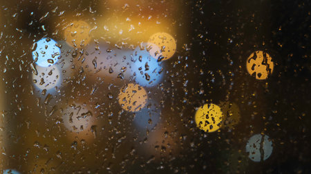 Close-up of the blurred light spots through the window and raindrops falling down on the glass at the evening. Concept. Rainy weatherの写真素材