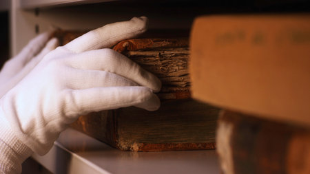 Close-up of hand in white cotton glove taking very old book from the bookshelf in museum or private library. Stock footage. Exploring of the ancient yellowed booksの写真素材
