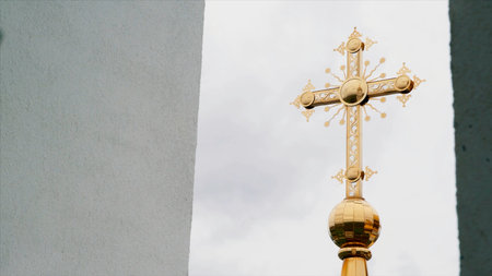 Religion and faith concept, bottom view of a golden cross of the church. Video. Big golden cross on cloudy sky background.の写真素材