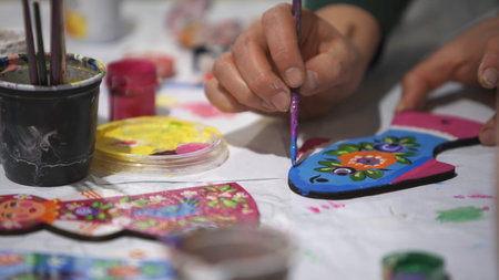 Close up of hands coloring flat figure at the workshop. Clip. Making traditional russian ornament with colorful paints on flat toys, lifestyle, hobby and art concept.の写真素材