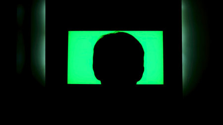 Rear view of a male head silhouette in front of tv with green screen. Concept. Man watching TV with chromakey that hanging on the wall at night at home.の写真素材