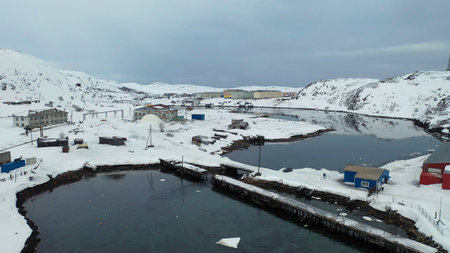 Aerial view of a long river flowing through the small village surrounded by snowy fields in winter season. Footage. Flying above white meadows, buildings, and calm river.の写真素材