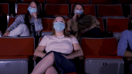 Cinema, entertainment, pandemic, and social distance concept. Media. People wearing face protective medical masks for prevention of virus disease watching movie in theater.の写真素材