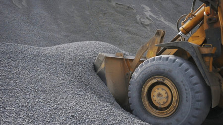 The tractor collects a scoop with gravel. Stock footage. Side view of an excavator loading its...