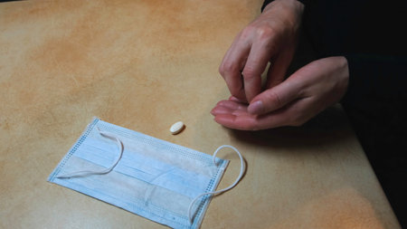 Woman hands putting white anti virus pills on the table with medical protective face mask and glass of water. Concept. Prevention of coronavirus illness.の写真素材