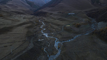 Dry autumn valley with river and mountains on the background. Footage. Aerial view of a curving stream flowing along yellow mountains slopes and a lonely house.の写真素材