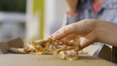 Close up of a young women hands taking pizza outdoor in the street. Media. Focus moving from hand to the slice of bbq pizza at the outdoor terrace of street cafe.の写真素材