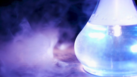 Close up of glass transparent flask of hookah on the table with a cloud of smoke. Media. Shisha flask under the blue lamp light standing on a wooden table.の写真素材