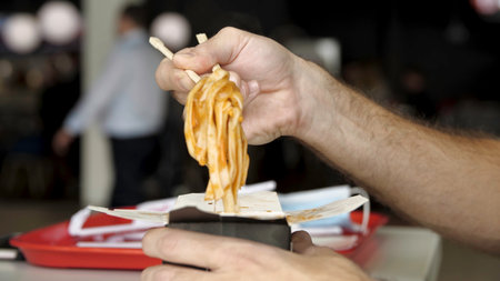 Close up of male hands with wooden chinese chopsticks eating delicious asian wok noodles. Media. Side view of eating chinese pasta in a public place.の写真素材