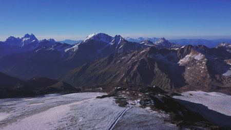 Aerial view of breathtaking high range of mountains on blue sky background. Clip. Flying over the giant hills with snowy peaks on a sunny day.の写真素材