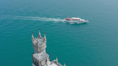 Castle on background of yacht in blue sea. Action. Top view of beautiful white castle near sea cliff...
