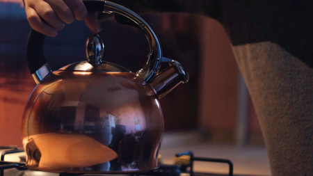 Woman taking teapot from the gas stove in the kitchen. Concept. Close up of young female turning off the flaming gas stove and takes away a metal kettle.の写真素材